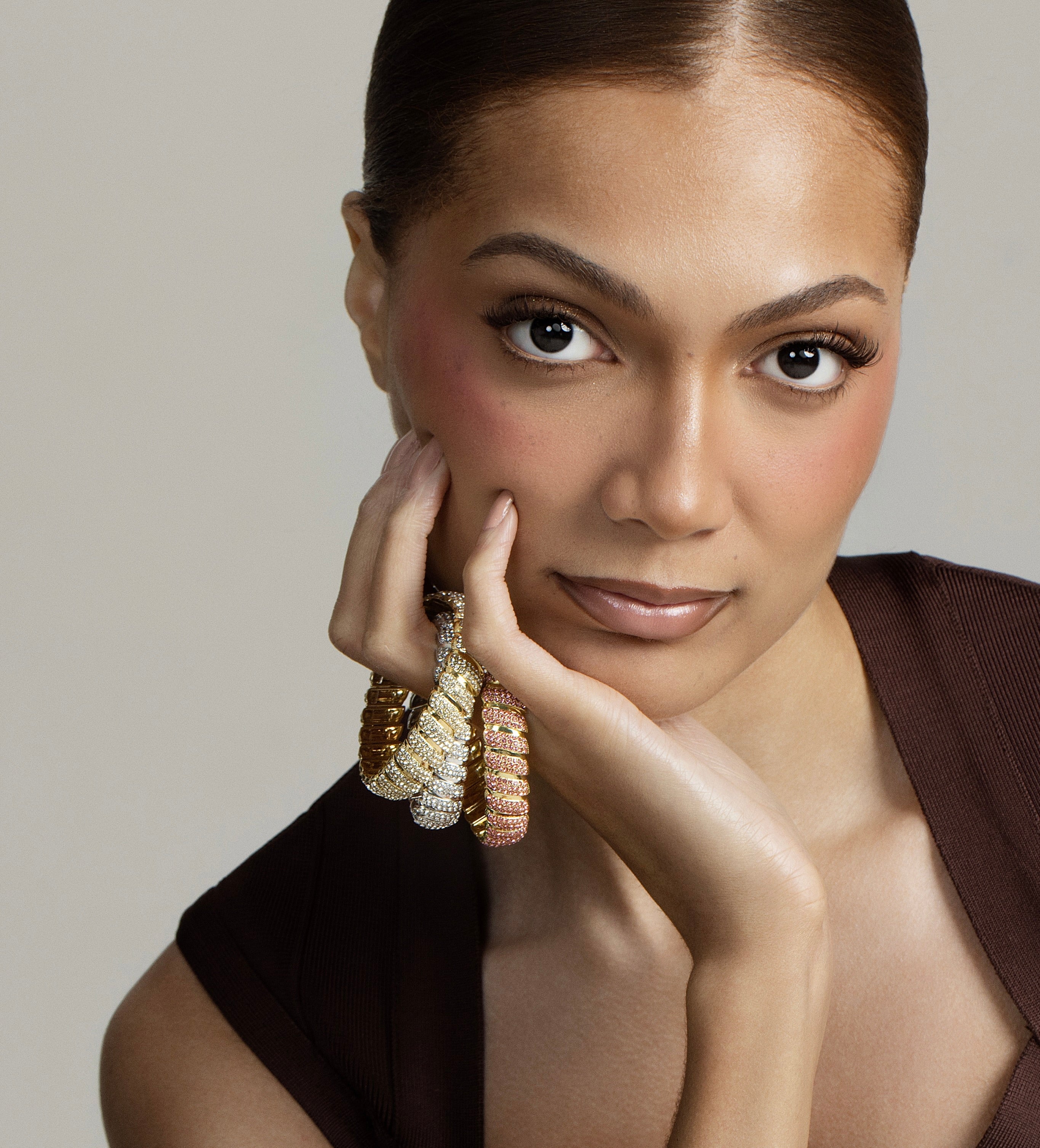 A beautiful model hold three pieces of our lustre twist collection with her hands on her face sitting on her wrist